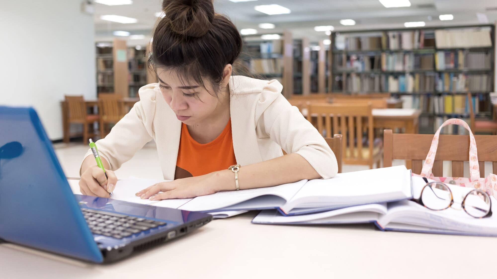 Studentka pisze w bibliotece przy laptopie i otwartych książkach