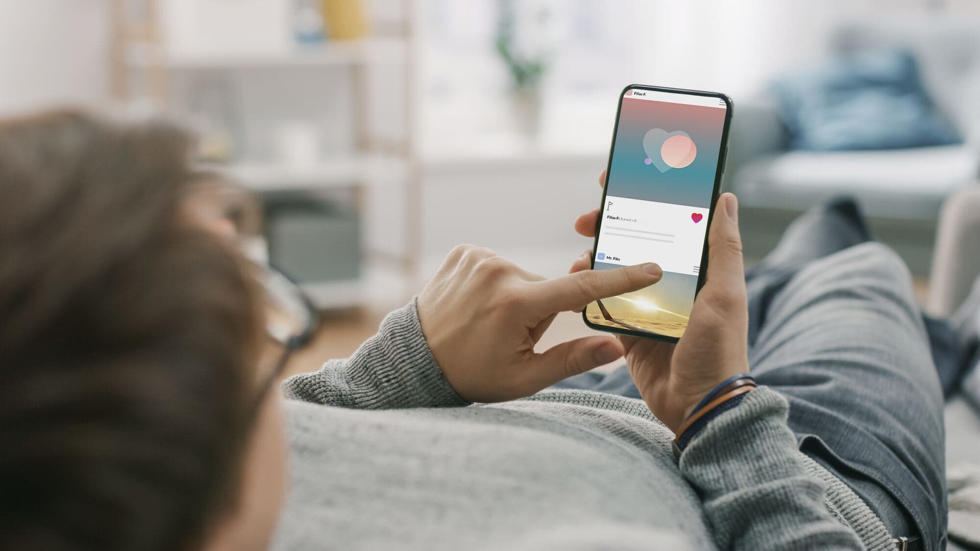 Osoba leży na kanapie i przewija ekran telefonu