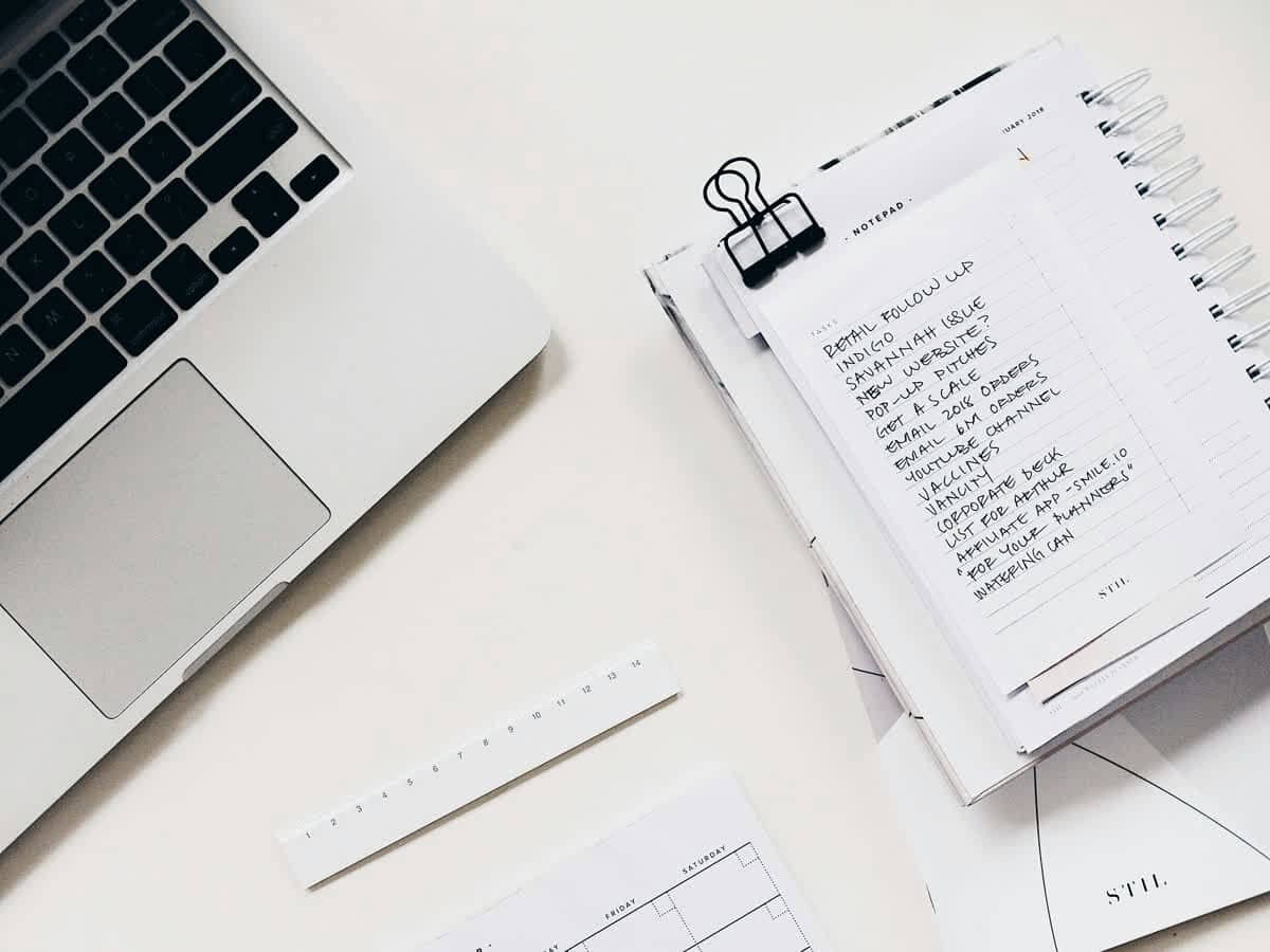 Białe biurko z laptopem, odręczną listą zadań w notesie i papierowym planerem
