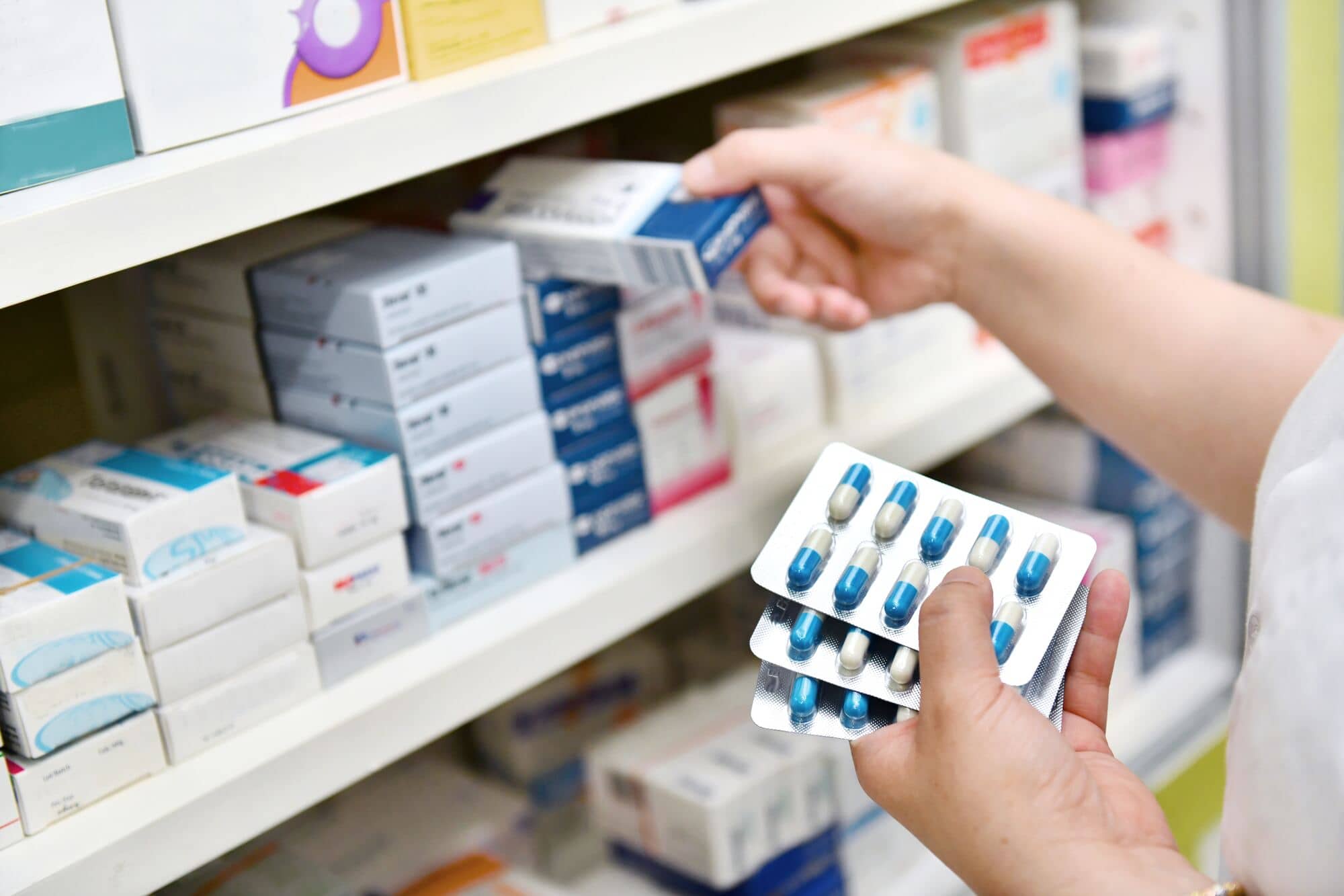 Farmaceutka trzyma opakowanie leku i blister kapsułek przy półkach apteki