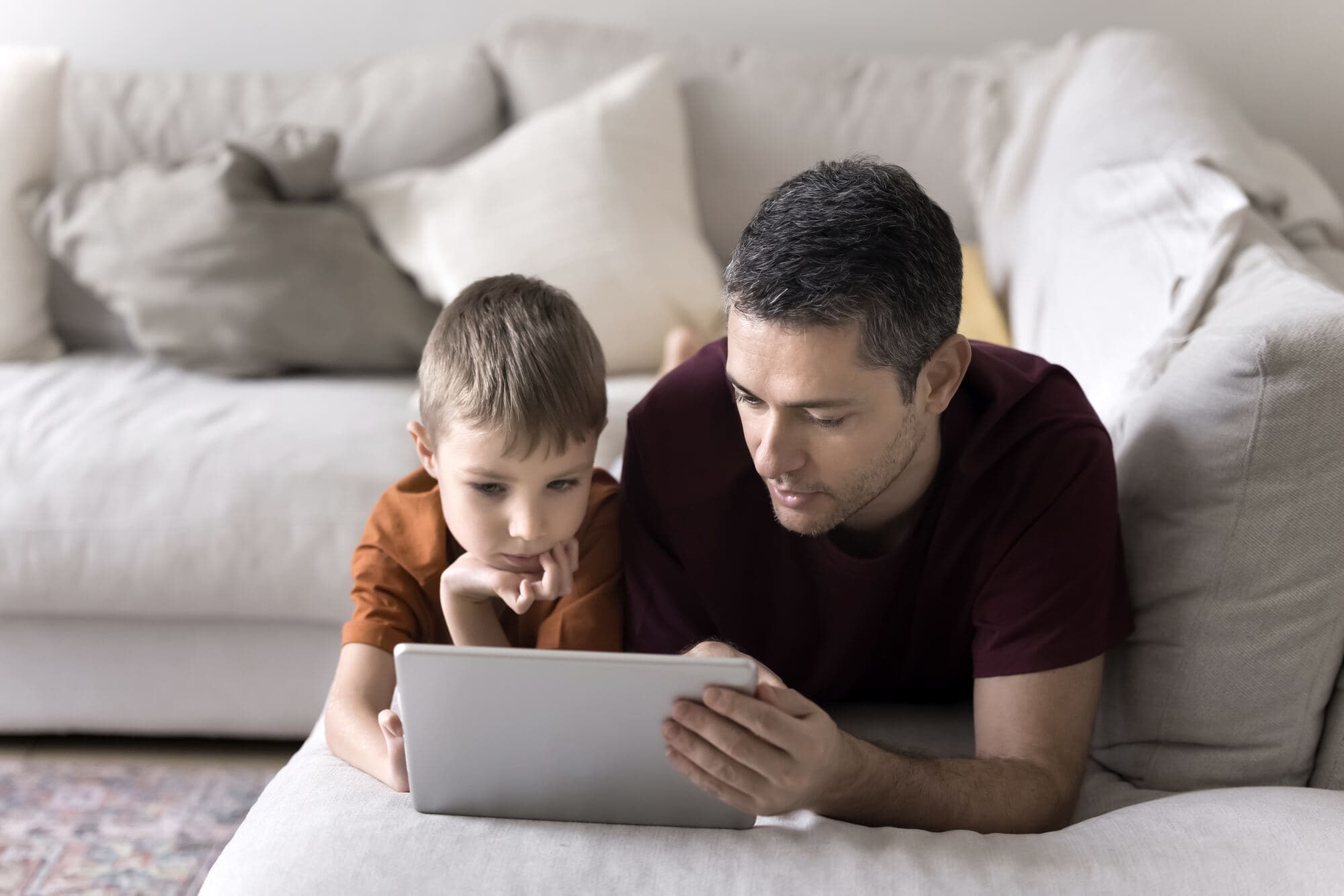 Ojciec z synem patrzą w tablet na kanapie