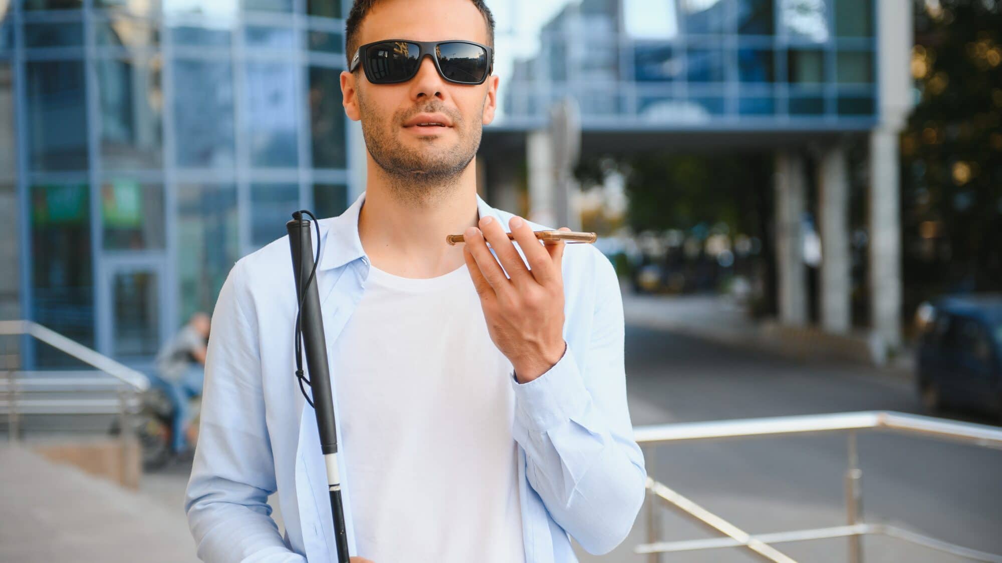 Niewidomy mężczyzna z białą laską mówi do telefonu na ulicy